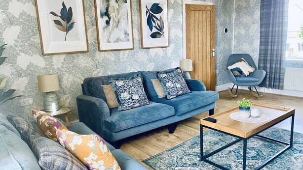 Una sala de estar con un sofá azul, una mesa de centro de madera y un tapiz estampado.