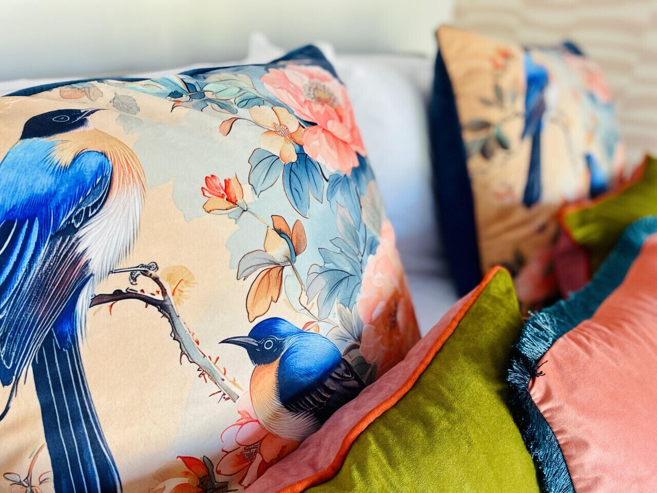 A bed with floral and bird-patterned bedding, multiple pillows, and a green and orange throw blanket.