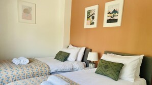 Habitación de hotel con dos camas, cada una con ropa de cama y almohadas estampadas, una mesita de noche con lámpara y obras de arte en las paredes.