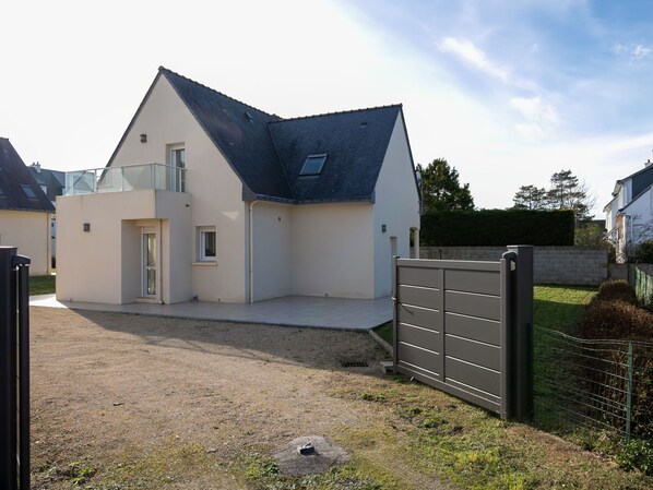 Une maison moderne à deux étages, dotée d’un toit en pente, d’un porche couvert et d’une allée menant à une porte grillagée.