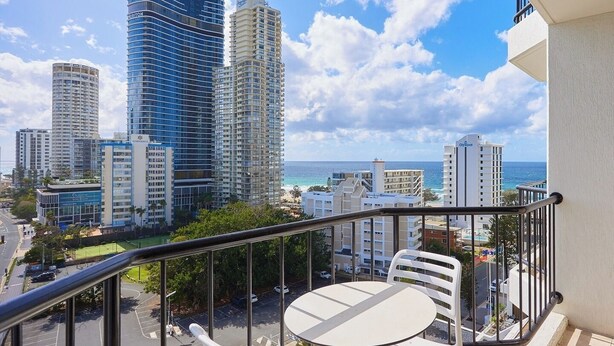 Un balcon avec une table et des chaises, donnant sur un paysage urbain avec de hauts immeubles et une plage.