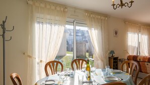Ein Essbereich mit Tisch für vier Personen, Stühlen, einer Kronleuchter und Blick in den Garten durch große Fenster.