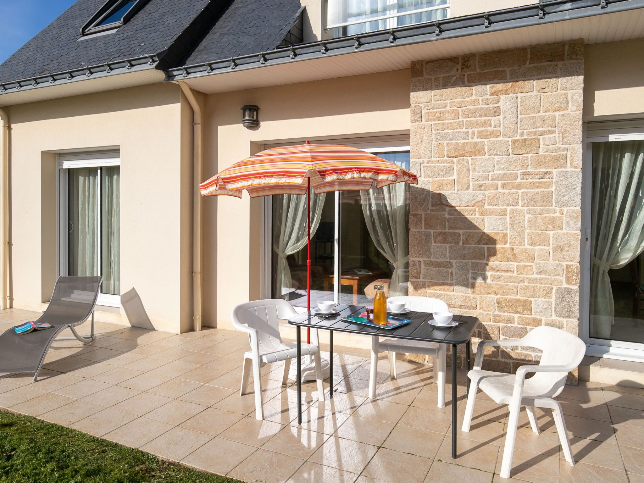 Une terrasse avec une table et des chaises, un parasol à rayures et un mur en pierre.