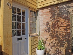 A wooden door with a window, a potted plant, and a brick wall with shadows.