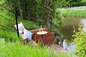 Una terraza de madera con una mesa y sillas, con vista a una masa de agua rodeada de vegetación.