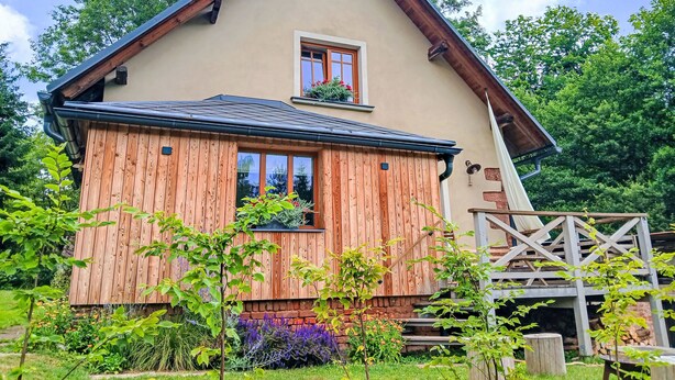 A two-story house with a wooden facade, a small balcony, and a garden with various plants. - Vidochov by Interhome (Nova Paka)