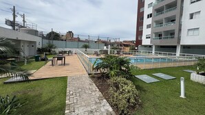 Un espace piscine aménagé sur le toit, avec une terrasse en bois, des chaises longues et un petit jardin.