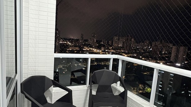 Un balcon avec deux chaises, un sol carrelé de carreaux blancs et une vue sur la ville illuminée la nuit.
