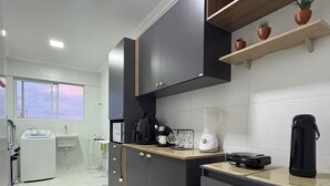 Une cuisine moderne avec des meubles gris, une machine à café et un four à micro-ondes. Une fenêtre offre une vue sur les bâtiments environnants.