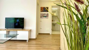 Un salon moderne avec un téléviseur à écran plat, une table basse en verre et un plancher en bois.