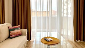 Un salon moderne avec un canapé, une table basse en verre et une vue dégagée à travers des rideaux légers.