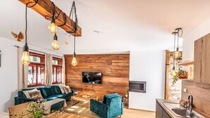 A modern living room with a wooden wall, a TV mounted above a fireplace, and a kitchen area with a sink and cabinets. - Apartment Lipno by Interhome (Horni Plana)