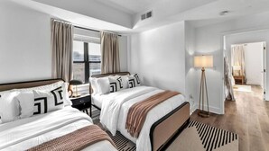 Una habitación de hotel moderna con dos camas, un ventanal con cortinas, una lámpara de pie y vistas a la ciudad.