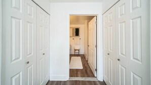 Un pasillo con puertas blancas, suelo de madera y una pequeña mesa con alfombra blanca.