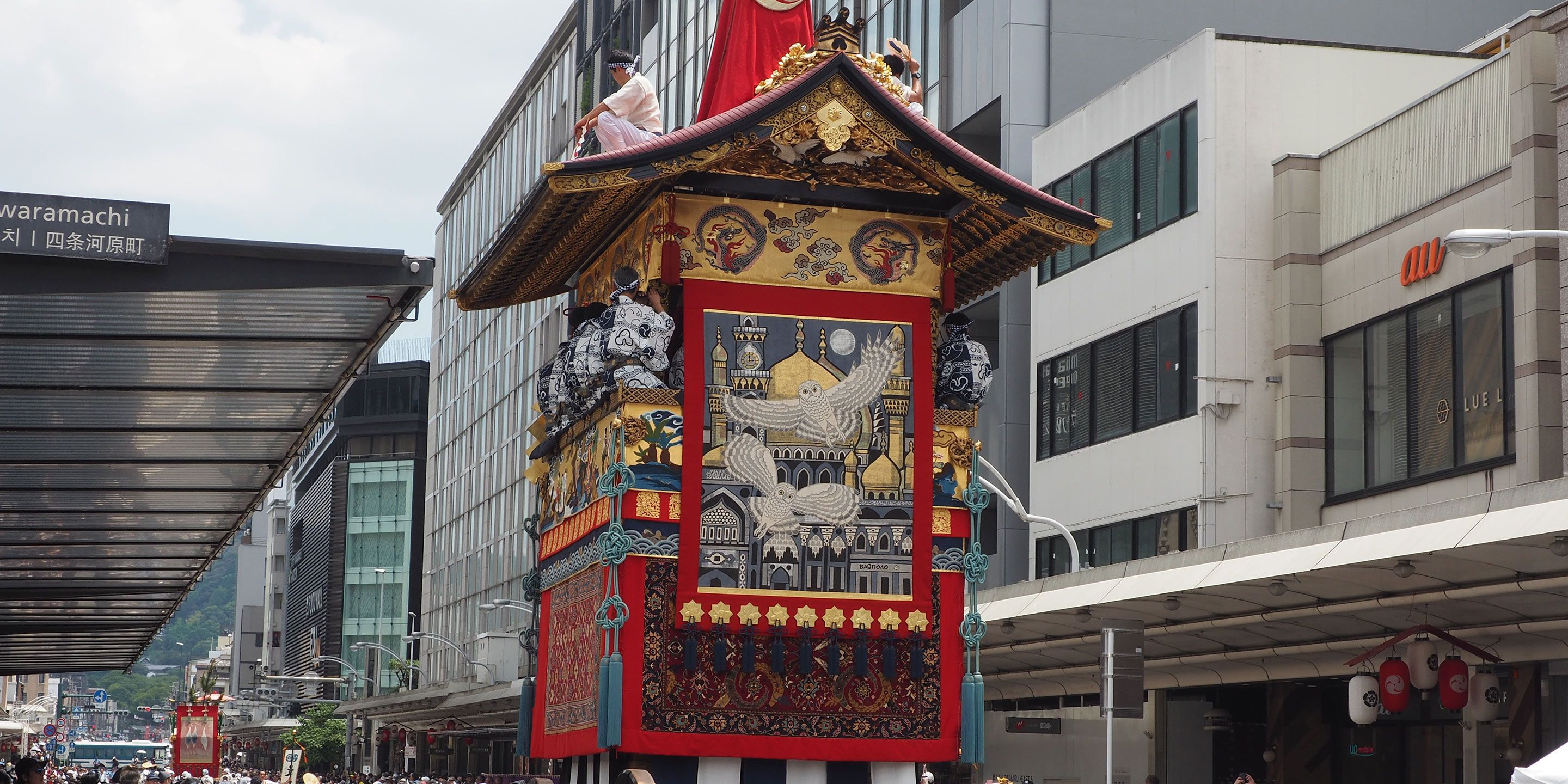Il s’agit d’une structure architecturale chinoise traditionnelle, caractérisée par des motifs complexes et une palette de couleurs rouge et or, située dans un environnement urbain, avec des bâtiments modernes en arrière-plan.