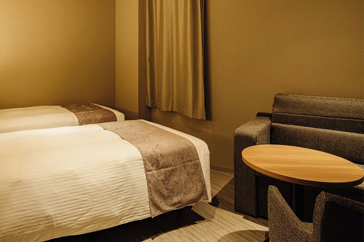 Habitación de hotel con dos camas, una mesita redonda y un rincón de descanso.