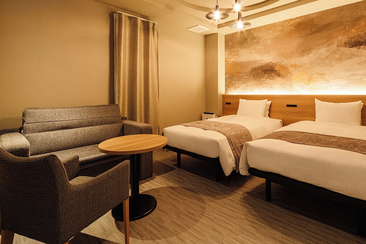 Habitación de hotel con dos camas, un sofá, una pequeña mesa redonda y un cuadro abstracto grande en la pared.