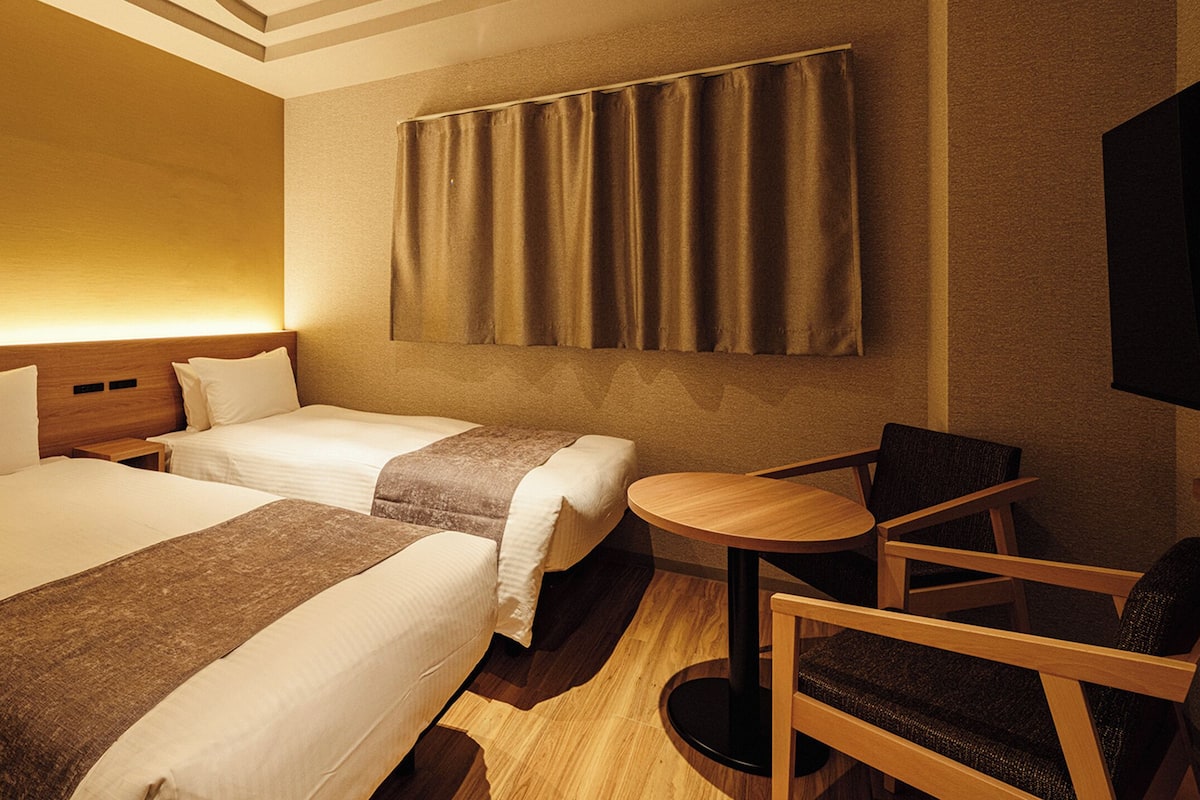 Habitación de hotel con dos camas, una mesita redonda y una sola silla.