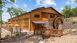 Een houten lodge met een waterrad, stenen muren en een terras met parasols.