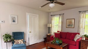 A living room with a blue armchair, a red sofa, a wooden coffee table, and a ceiling fan. - Mariam's On Becket (Salem)