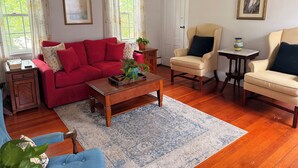 A living room with a red sofa, beige armchairs, a wooden coffee table, and a blue rug. - Mariam's On Becket (Salem)
