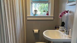 A bathroom with a toilet, sink, window, and shower curtain. - Mariam's On Becket (Salem)