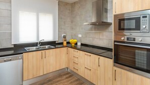 A modern kitchen with wooden cabinets, a stainless steel microwave, and an oven. - Vacation home Esteva by Interhome (Maçanet de la Selva)
