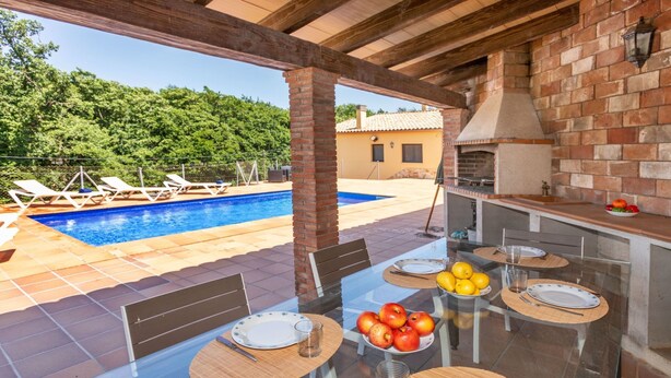 An outdoor dining area with a glass table, chairs, and a view of a swimming pool and greenery. - Vacation home Esteva by Interhome (Maçanet de la Selva)