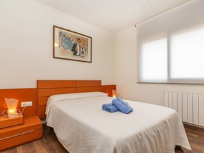 A hotel room with a bed, a nightstand with a lamp, a framed picture on the wall, and a window providing natural light.