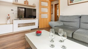 A modern living room with a grey sofa, a white coffee table with wine glasses, a TV on a white cabinet, and a painting on the wall. - Vacation home Esteva by Interhome (Maçanet de la Selva)