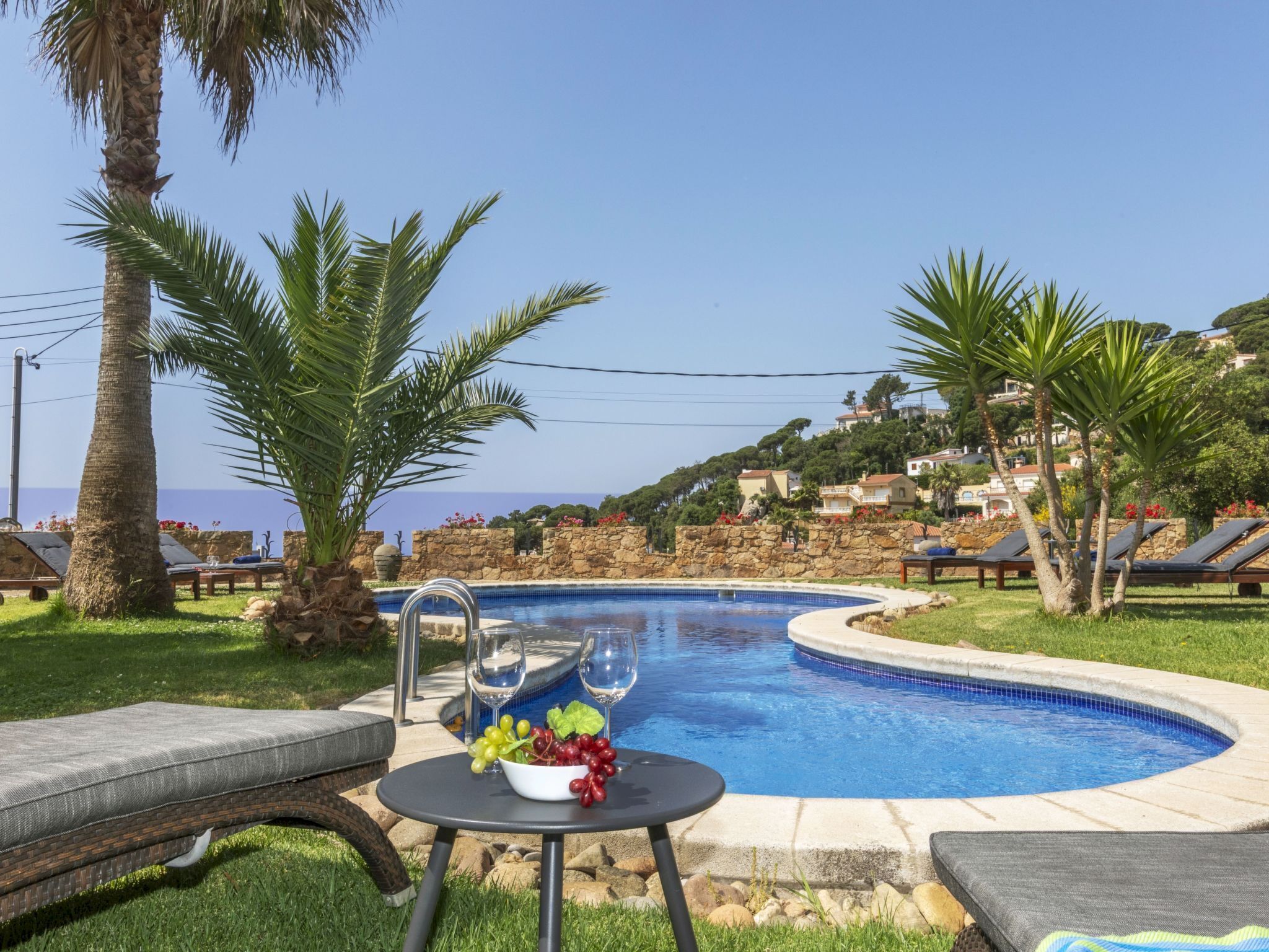 A pool area with lounge chairs, a table with a bowl of fruit, and a view of the sea and hills in the background.