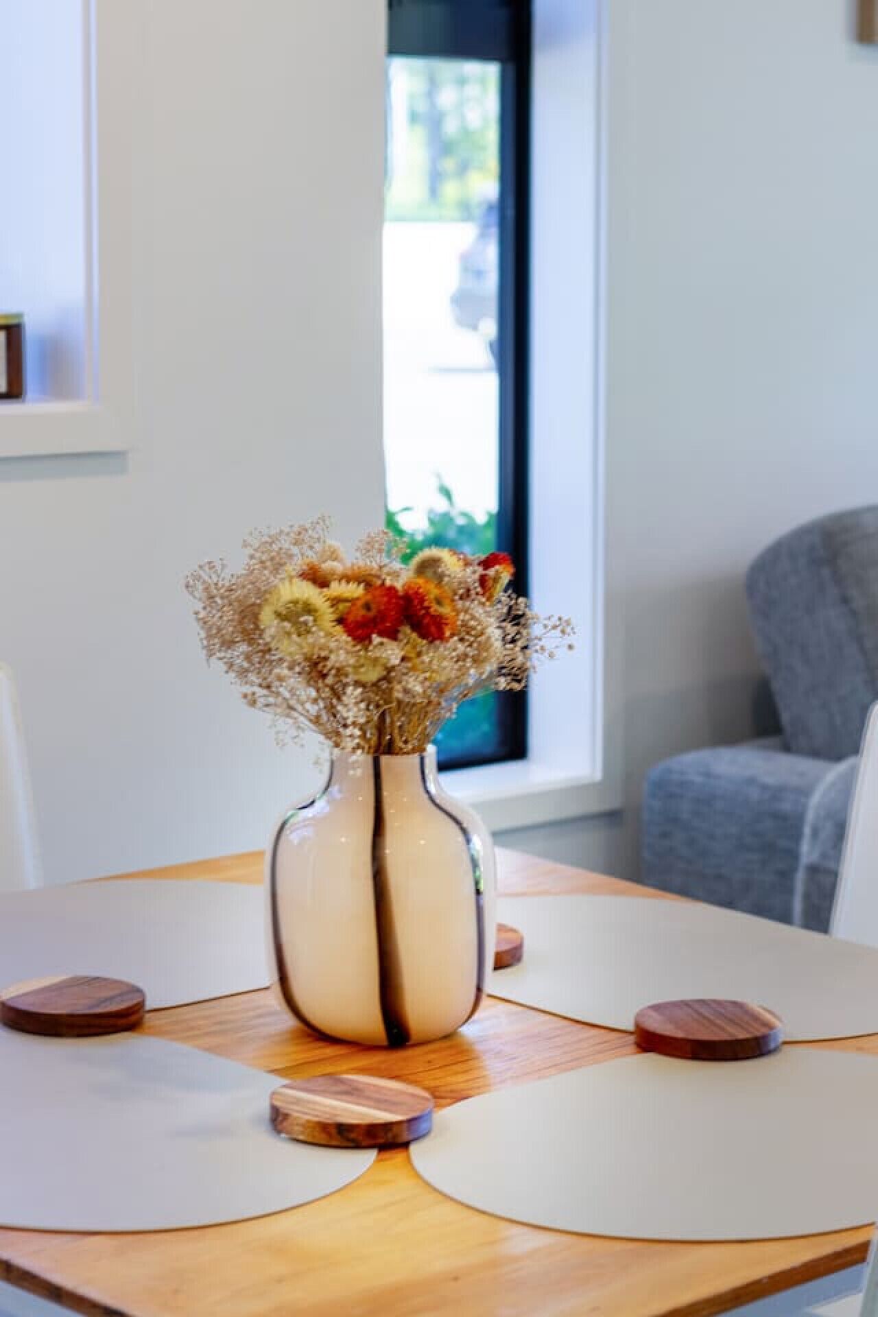 A round wooden table with a vase of flowers and coasters.