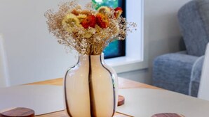 Una mesa redonda de madera con un jarrón de flores y posavasos.