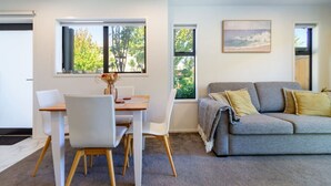 Una sala de estar moderna con un sofá gris, sillas blancas y una mesa de comedor de madera.
