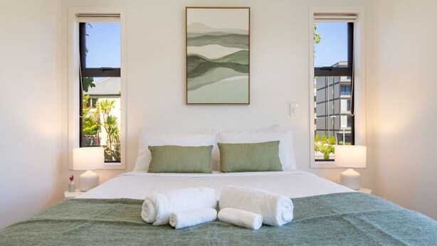 Una cama bien hecha con dos almohadas, una colcha verde y dos toallas enrolladas sobre la cama.