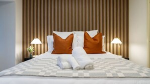 Ein ordentlich gemachtes Bett mit einer karierten Tagesdecke, zwei Kissen und zusammengerollten Handtüchern.
