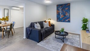 Ein modernes Wohnzimmer mit einem dunklen Sofa, einem runden Couchtisch und einem Essbereich mit einem Holztisch und Stühlen.