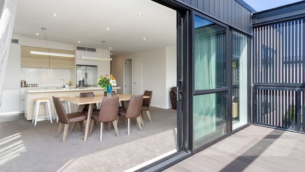 A modern kitchen with a central island, a dining area with a table and chairs, and a sliding glass door leading to an outdoor space.
