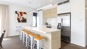 A modern kitchen with a central island, stainless steel appliances, and bar stools.