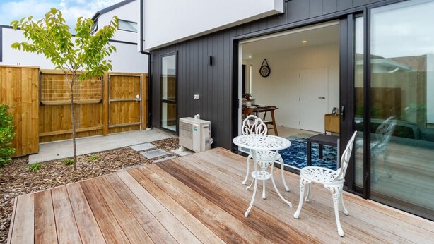 Eine moderne Terrasse im Freien mit Holzdeck, weißem Metalltisch und -stühlen sowie einem kleinen Baum.