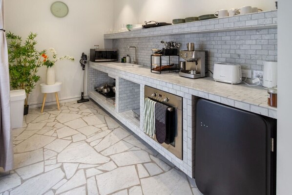 A modern kitchen with a stone tile floor, built-in oven, microwave, and a coffee machine.