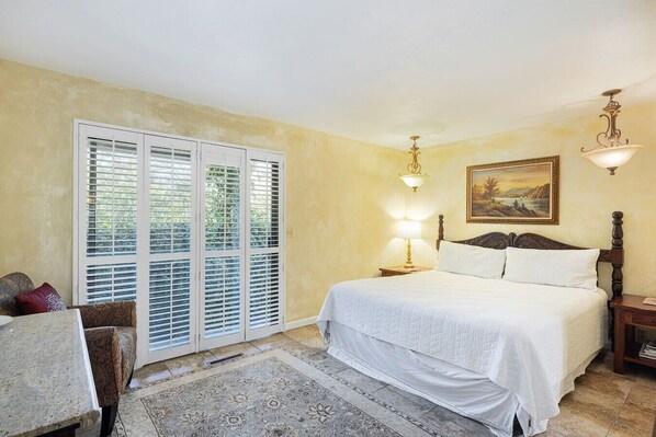 A bedroom with a bed, a nightstand, a lamp, a chair, and a window with blinds.