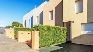 A row of modern, single-story buildings with a uniform facade, a paved driveway, and a well-maintained hedge. - Bousquet by Interhome (L'Escala)