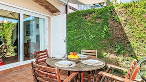 An outdoor patio with a round wooden table set for dining, surrounded by wooden chairs. - Bousquet by Interhome (L'Escala)