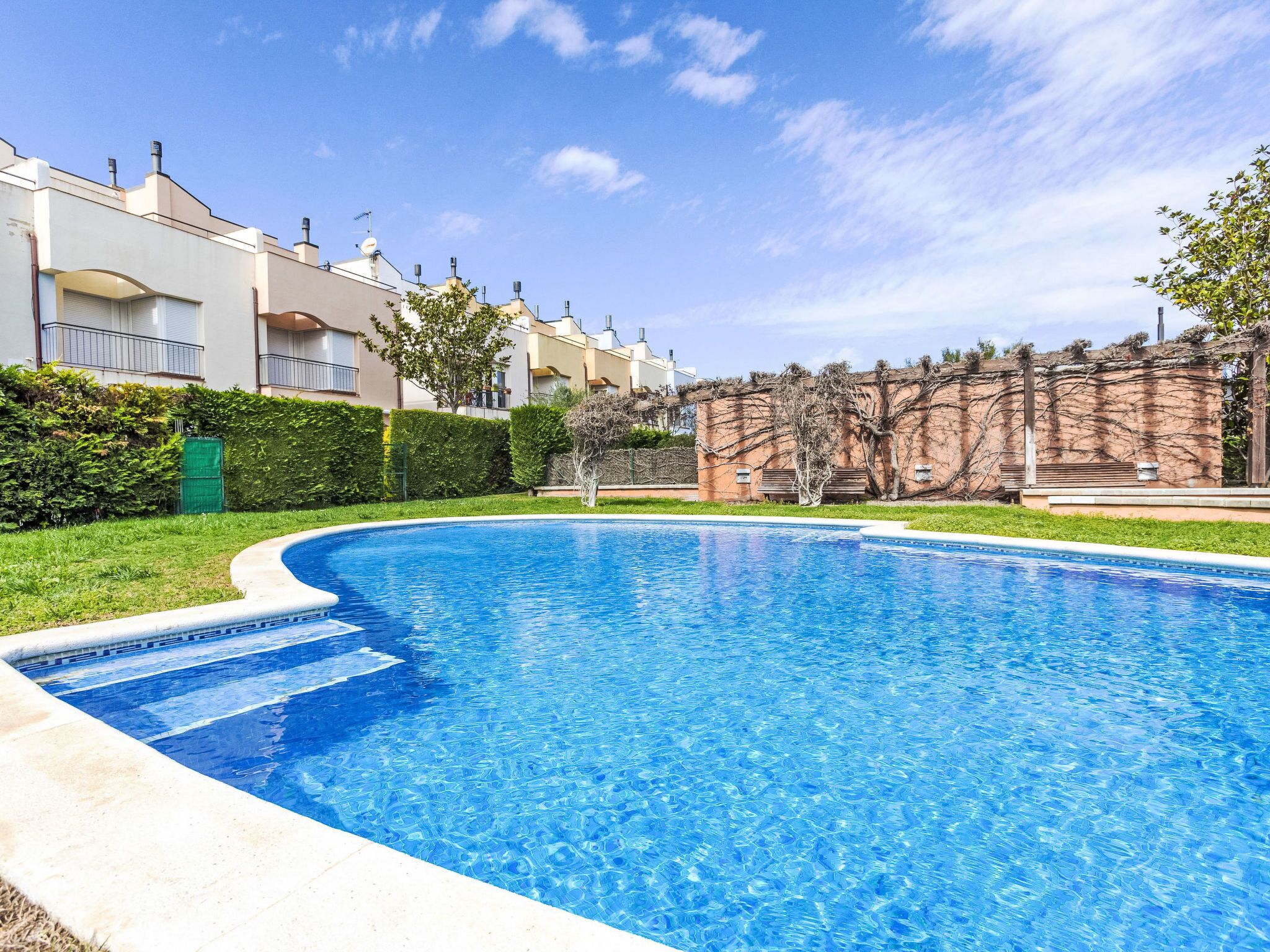Une piscine entourée d’un jardin bien entretenu et bordée d’une rangée d’immeubles d’habitation.