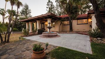 A courtyard with a fountain, stone pathway, and a house with a tiled roof and columns.