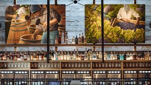 A bar with a wooden interior, shelves of liquor bottles, and two large paintings depicting winemaking scenes. - Villa Terra Bella, by Vinifera Homes (Windsor)