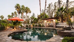A pool area with stone paving, palm trees, and a red umbrella. - Villa Terra Bella, by Vinifera Homes (Windsor)