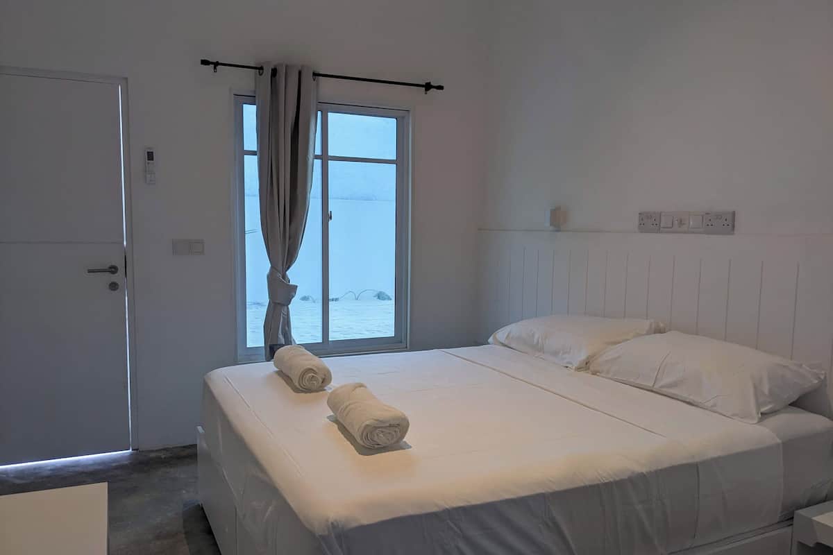 A hotel room with a bed, a window with curtains, a door, and a bedside table.