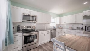 A modern kitchen with white cabinets, stainless steel appliances, and a wooden dining table.